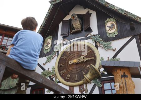 28. Oktober 2022, Sachsen-Anhalt, Gernrode: Ein Junge schaut auf dem Gelände der ehemaligen Harzer Uhrenfabrik in Gernrode aufmerksam auf die größte Kuckucksuhr außerhalb des Schwarzwaldes. Rund 300 verschiedene Kuckucksuhren und weitere Exponate werden hier auf 800 Quadratmetern präsentiert. Das Uhrenmuseum umfasst auch einen Werkstattbereich, in dem Kuckucksuhren und andere Uhrwerke fachmännisch repariert werden. Hauptattraktion des Museums ist die größte Kuckucksuhr außerhalb des Schwarzwaldes mit einer Höhe von 14,50 Metern. Am letzten Sonntag im Oktober beginnt die sogenannte Winterzeit. In der Nacht von Samstag auf Sonntag Stockfoto