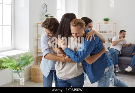 Gesellschaft von fröhlichen Freunden, die glücklich sind, einander während des Treffens zu Hause umarmen zu sehen. Stockfoto