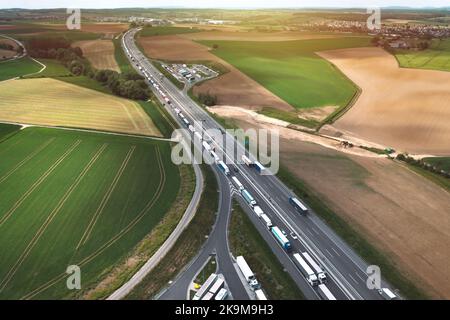 Luftaufnahme des logistischen Verkehrs und Parkplätze voll von Lastwagen auf der Autobahn mit Feldern in Polen. Blick von der Drohne. Stockfoto