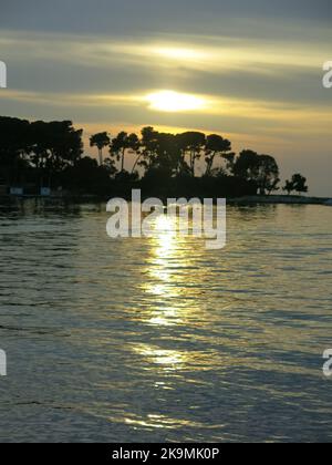 Ein wunderschöner Sonnenuntergang an der Küste der istrischen Halbinsel; eine romantische Kulisse mit Bäumen auf einer Insel in dunkler Umrisse gegen die untergehende Sonne. Stockfoto