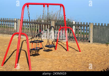 Schaukeln für kleine Kinder in einem Park oder Spielplatz. Leere Schaukeln. Blauer Himmel im Sommer. Weicher Boden unter den Spielschaukeln zur Sicherheit. Stockfoto