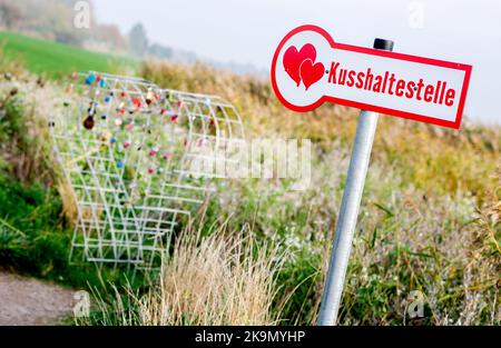 Wangerland, Deutschland. 29. Oktober 2022. Ein Schild mit der Aufschrift 'Kissing stop' steht in einem Feld neben einem Drahtgeflecht, das für sogenannte Liebesschlösser bestimmt ist. In der Nähe des Dorfes Bassens in der Gemeinde Wangerland können Liebhaber in diesem Rastplatz am Straßenrand für einen Kuss und gemeinsame Momente anhalten und sich mit einem von ihnen mitgebrachten Liebesschloss verewigen. Quelle: Hauke-Christian Dittrich/dpa/Alamy Live News Stockfoto
