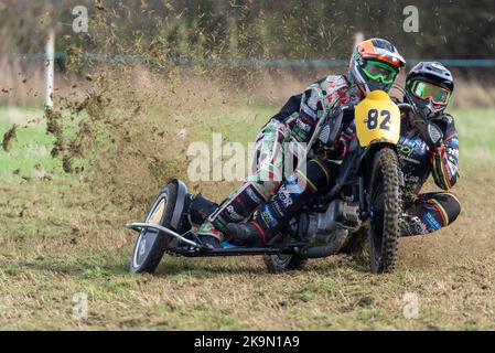 Purleigh Barns Farm, Latchingdon, Essex, Großbritannien. 29. Oktober 2022. Solo- und Seitenwagen-Motorräder sowie Quad-Bikes fuhren in verschiedenen Klassen auf einem Feld in der Nähe von Maldon in Essex um eine schlammige ovale Rennstrecke, organisiert vom Southend & District Motorcycle Club. Grasstrack-Rennen ist ähnlich wie Speedway-Rennen. Die Wettkampfklassen variieren zwischen im Uhrzeigersinn und gegen den Uhrzeigersinn. Die Motorleistung reicht bis zu 1000cc und umfasst Vintage-Maschinen vor 1975. 82 - Benjamin Ilsley und Luke Russell in der Seitenwagenklasse 500cc Stockfoto