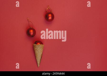 Neujahrskugeln in einem Waffelkegel auf rotem Hintergrund. Runde Spielzeuge mit Goldfaden. Alternative Konzept der Feier Winterferien, top V Stockfoto