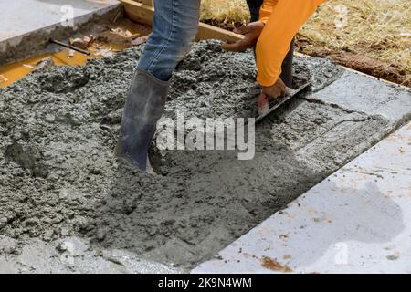 Der Mason-Arbeiter hält eine Stahlkelle und glättet den neuen Gehweg auf nassem, frisch gegossenen Beton auf der Baustelle Stockfoto