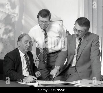 1989, historisch, in einem Büro, an einem Schreibtisch, versammelten sich drei Führungskräfte, die sich einen Unternehmensbericht, England, Großbritannien, angeschaut haben. Stockfoto