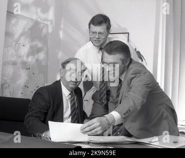 1989, historisch, in einem Büro, versammelten sich drei leitende Führungskräfte eines Unternehmens, um einen Bericht zu betrachten, England, Großbritannien. Stockfoto