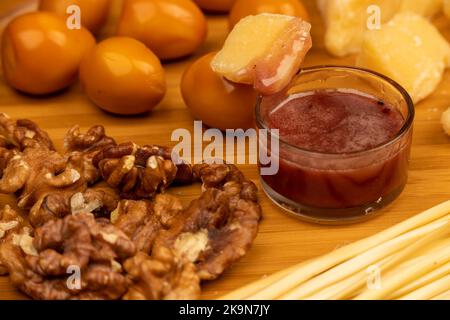 Verschiedene Sorten von Käse, Walnusskernen, geräucherten Wachteleiern und Honig in einer Glasvase auf einer Holzoberfläche. Stockfoto