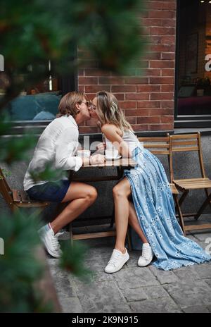 Hipster küsst Paar im Straßenrestaurant. Romantisches Paar haben Frühstück und Kaffee draußen. Stilvolle Frau und modischer Mann aus dem Straßencafé Stockfoto