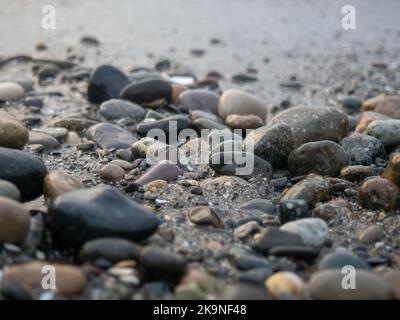 Kieselsteine an der Küste aus der Nähe. Felsiger Strand. Steine Nahaufnahme mit Bokeh. Grauer natürlicher Hintergrund. Das Konzept der Erholung an der Küste. The Velvet se Stockfoto