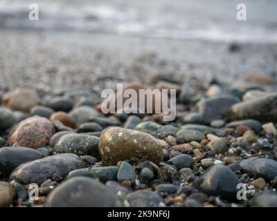 Kieselsteine an der Küste aus der Nähe. Felsiger Strand. Steine Nahaufnahme mit Bokeh. Grauer natürlicher Hintergrund. Das Konzept der Erholung an der Küste. The Velvet se Stockfoto