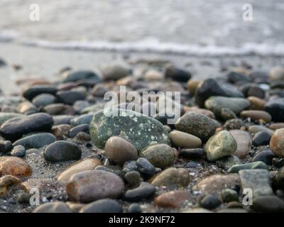 Kieselsteine an der Küste aus der Nähe. Felsiger Strand. Steine Nahaufnahme mit Bokeh. Grauer natürlicher Hintergrund. Das Konzept der Erholung an der Küste. The Velvet se Stockfoto