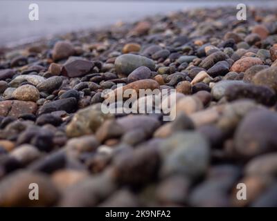 Kieselsteine an der Küste aus der Nähe. Felsiger Strand. Steine Nahaufnahme mit Bokeh. Grauer natürlicher Hintergrund. Das Konzept der Erholung an der Küste. The Velvet se Stockfoto