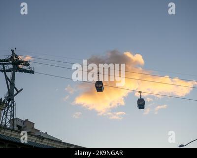 Seilbahn. Esaltor steht vor dem Hintergrund einer goldenen Wolke. Eine Wolke über der Stadt in einer ungewöhnlichen Farbe. Silhouetten von Seilbahnkabinen in der sk Stockfoto