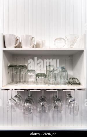 Nahaufnahme der modernen Küche Zimmer Innenarchitektur weißen Schrank Regale mit weißen Tassen, auf dem Kopf hängend leere Weingläser Rack zur Aufbewahrung Stockfoto