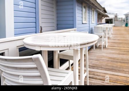 Am Meer mit leeren Stühlen Barhocker, runde Holztische im Winter Florida Panhandle Stadt Stranddorf mit weiß blau Architektur Restaurant Stockfoto