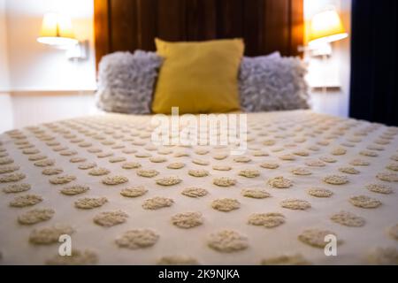 Werfen Sie am Abend dekorative Kissen, eine tuftete Daunendecke auf das Bett im Schlafzimmer mit weichem Bezug und moderne Nachttischlampen, die im Hotel oder zu Hause beleuchtet werden Stockfoto