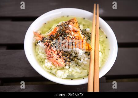 Makro-Nahaufnahme von traditionellen japanischen asiatischen Gerichten mit Ochazuke mit gegrilltem Lachs, Reissesamsamen-Furikake, Nori in weißem Schüssel-Teller, Essstäbchen Stockfoto