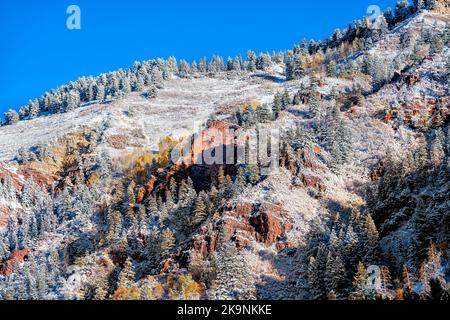 Nahaufnahme der Maroon Bells Gegend in Aspen, Colorado mit orangen felsigen Bergklippen, die nach dem Winter im Herbst mit Schnee bedeckt sind, Kiefernfichtenwald Stockfoto