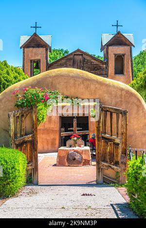 Berühmte historische Sanktuar-Kirche El Santuario de Chimayo in den Vereinigten Staaten mit Eingangstor durch Blumen im Sommer Stockfoto