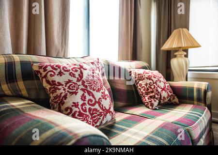 Karierte karierte Sofa-Couch mit altmodischem Retro-dekorativem Kissen, Lampe am Nachttisch am Fenstervorhang im Wohnzimmer der alten Hütte Stockfoto