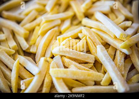 Makro-Nahaufnahme von gefrorenen, rohen, gerade geschnittenen, salzigen pommes Frites, die Pommes Frites auf dem Backblech vor dem Kochen oder Braten mit Texturdetails aufkochen Stockfoto