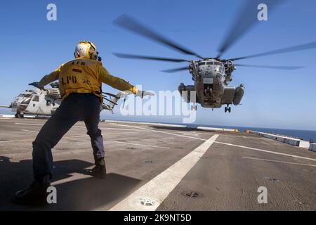 Der Flugzeugführer Mate (Handling) von Aviation Boatswain leitet einen CH-53E Super-Hengst-Hubschrauber, der dem Marine Heavy Helicopter Squadron (HMH) 465 zugewiesen wurde, um auf dem Flugdeck des Amphibientransportschiffes USS John P. Murtha (LPD 26) zu landen. Stockfoto