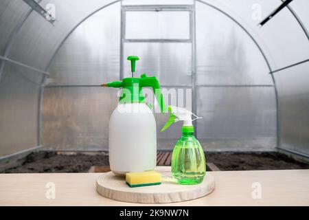 Greenhouse-Reinigungsprodukte auf dem Tisch, Stillleben. Reinigen und Waschen im Inneren des leeren Gewächshauses mit einer antibakteriellen Reinigungsflüssigkeit. Stockfoto