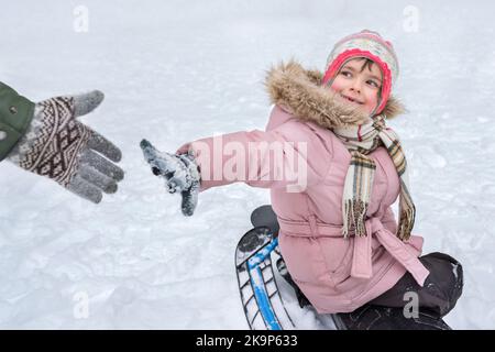 Das kleine Mädchen an einem verschneiten Tag gibt seinem Vater die Hand. Ein Kind spielt im Winter auf der Straße Stockfoto