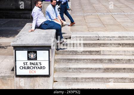 London, Großbritannien - 22. Juni 2018: Junge Geschäftsleute sitzen während der Mittagspause in der City of London auf dem Kirchhof der St. Paul's Cathedral Stockfoto