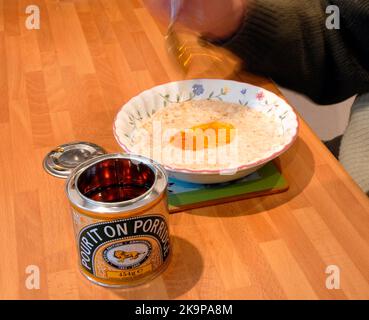 Gericht aus Haferbrei, mit einer Dose goldenem Sirup, wobei Sirup mit einem Löffel auf den Haferbrei gelegt wird Stockfoto