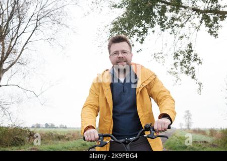 Mann in einem gelben Windbreaker auf einem Fahrrad an einem nebligen Morgen. Aktives Wochenende und gesunder Lebensstil. Stockfoto