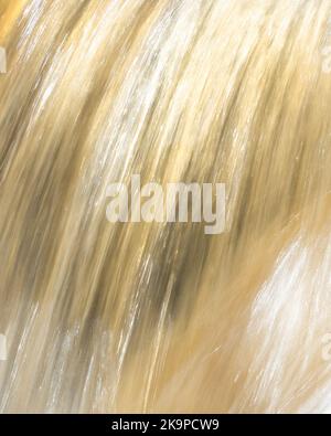 Nahaufnahme von Wasser schimmerndem Gold, wie es über Felsen in kleinen Wasserfall fließt, der von niedriger Sonne beleuchtet wird Stockfoto