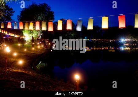 Horumersiel, Deutschland. 29. Oktober 2022. Zahlreiche bunte Laternen hängen an einer Linie um den natürlichen See Kolk im Stadtzentrum und spiegeln sich im Wasser. Hunderte von Laternen und Fackeln sowie schwebende Lichter in bunten Seerosen verwandeln den Kolk während der traditionellen Kolk-Beleuchtung in ein buntes Lichtermeer. Quelle: Hauke-Christian Dittrich/dpa/Alamy Live News Stockfoto