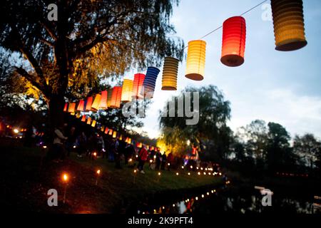 Horumersiel, Deutschland. 29. Oktober 2022. Zahlreiche bunte Laternen hängen an einer Linie rund um den Natursee Kolk im Stadtzentrum. Hunderte von Laternen und Fackeln sowie schwebende Lichter in bunten Seerosen verwandeln den Kolk während der traditionellen Kolk-Beleuchtung in ein buntes Lichtermeer. Quelle: Hauke-Christian Dittrich/dpa/Alamy Live News Stockfoto