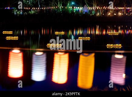 Horumersiel, Deutschland. 29. Oktober 2022. Zahlreiche bunte Laternen hängen an einer Linie um den natürlichen See Kolk im Stadtzentrum und spiegeln sich im Wasser. Hunderte von Laternen und Fackeln sowie schwebende Lichter in bunten Seerosen verwandeln den Kolk während der traditionellen Kolk-Beleuchtung in ein buntes Lichtermeer. Quelle: Hauke-Christian Dittrich/dpa/Alamy Live News Stockfoto