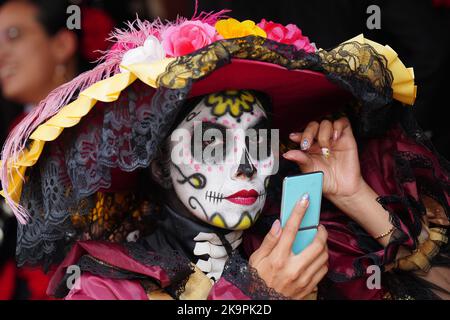 Mexiko-Stadt, Mexiko. 29. Oktober 2022. Eine Frau, die in das Kostüm der Skelett-Braut Catrina gekleidet ist, bereitet ihr Make-up vor dem Beginn der Großen Parade der Toten vor, um den Feiertag von Dia de los Muertos auf dem Paseo de la Reforma am 29. Oktober 2022 in Mexiko-Stadt, Mexiko, zu feiern. Quelle: Richard Ellis/Richard Ellis/Alamy Live News Stockfoto