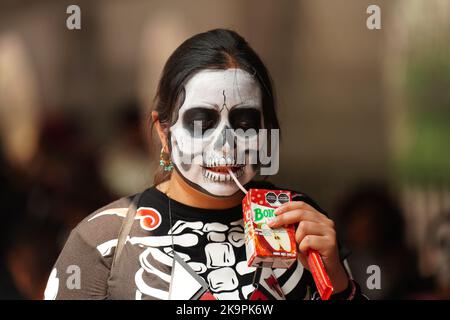 Mexiko-Stadt, Mexiko. 29. Oktober 2022. Eine Frau, die in das Kostüm der Skelett-Braut Catrina gekleidet ist, trinkt an einem heißen Tag einen Drink, bevor sie an der Großen Parade der Toten auftrat, um den Feiertag Dia de los Muertos auf dem Paseo de la Reforma am 29. Oktober 2022 in Mexiko-Stadt, Mexiko, zu feiern. Quelle: Richard Ellis/Richard Ellis/Alamy Live News Stockfoto