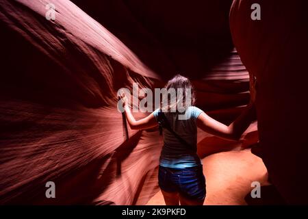 Junge Frau zurück im Upper Antelope Slot Canyon, Arizona, stehend, die Sandsteinfelsen zwischen den Wänden berührt Stockfoto