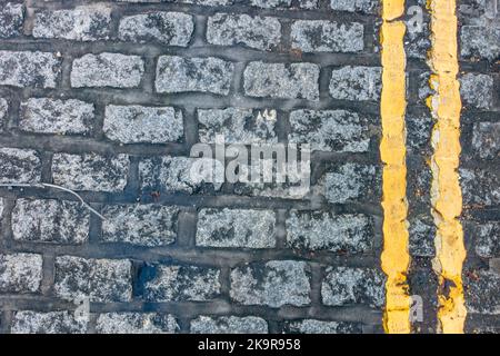Blick hinunter auf doppelte gelbe Linien entlang der Kante einer gepflasterten Straße gemalt. Stockfoto