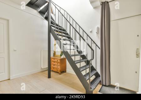 Vintage-Schrank mit Dekorationen und Spiegel in der Nähe offene Wohnzimmertür und Treppe im Flur des Hauses Stockfoto