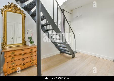 Vintage-Schrank mit Dekorationen und Spiegel in der Nähe der Treppe im Flur des Hauses Stockfoto