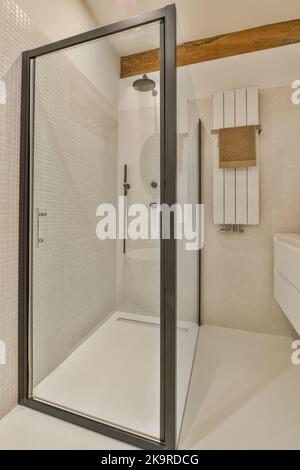 Badewanne mit Glasdusche in der Ecke neben Waschbecken und Spiegel im kleinen hellen Badezimmer mit weißen Kachelwänden Stockfoto