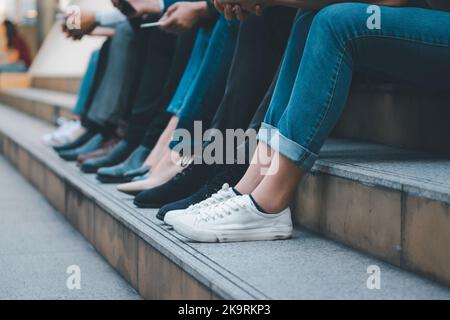 Gruppe von Gruppen verschiedener Leute, die zusammen an der Treppe sitzen, aus der Nähe an den Beinen. Stockfoto