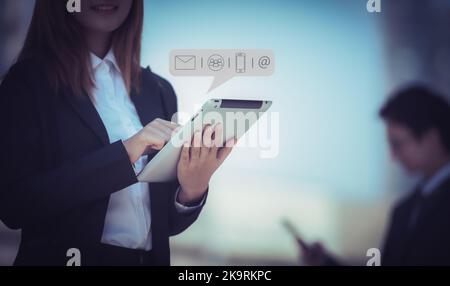 Hände einer Geschäftsfrau, die auf einem Tablet-Computer mit Symbol für Kommunikationskontakt, E-Mail, Telefonnummer, Social Media Group tippt. Kategorie Geschäft Stockfoto