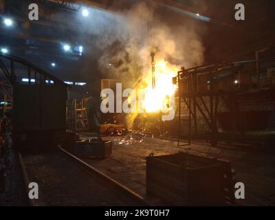 In einer Gießerei wird geschmolzenes Metall aus einem Ofen in eine Schöpfkelle gegossen Stockfoto