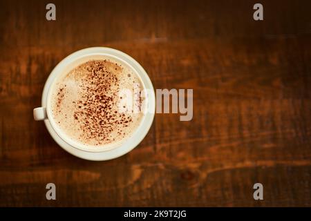 Dringend benötigt und sehr gesucht. Eine frisch gebrühte Tasse Kaffee, die in einem Restaurant auf einem Tisch neben dem eigenen steht, ist in einem hohen Winkel aufgenommen worden. Stockfoto
