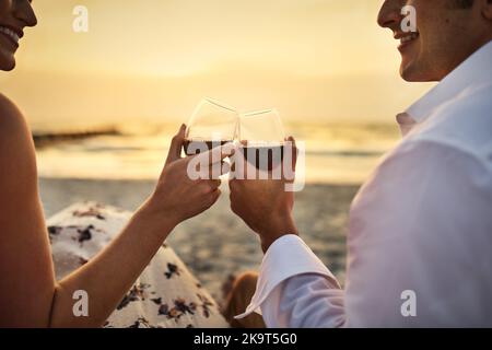 Für uns. Rückansicht eines liebevollen jungen Paares, das am Strand Wein genießt. Stockfoto