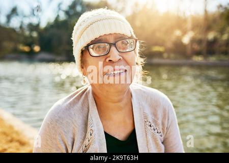 Älter werdende Tage wie diese sind umso mehr wichtig. Porträt einer älteren Frau, die neben einem See steht. Stockfoto