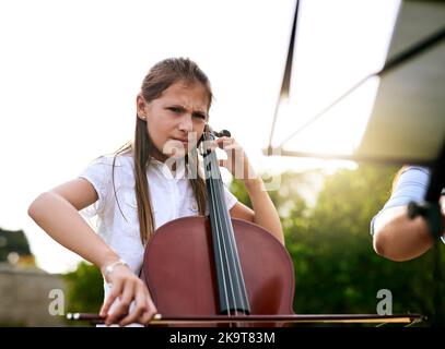 Entschlossen, eines Tages ein großartiger Musiker zu sein. Ein entschlossenes junges Mädchen, das tagsüber im Hinterhof ihres Hauses Cello spielt. Stockfoto